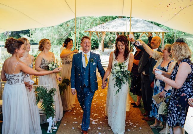 A couple walking through a marquee after being married with confetti being thrown on them