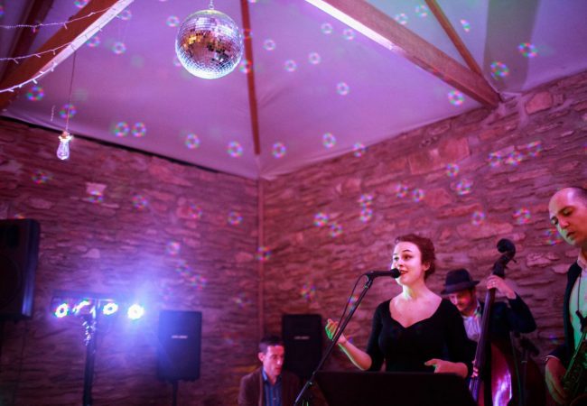 A band singing is a barn with a mirror ball